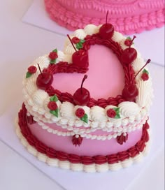 two heart shaped cakes with cherries on top, one is pink and the other is white