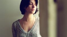 a woman standing in front of a mirror wearing a sweater and pearls on her necklace