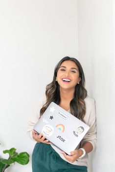 a woman holding a laptop with stickers on the cover and smiling at the camera