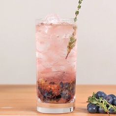 a tall glass filled with ice and blueberries on top of a wooden table next to berries