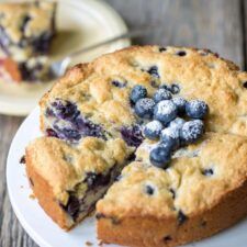 a blueberry cheesecake on a white plate with a slice cut out and ready to be eaten