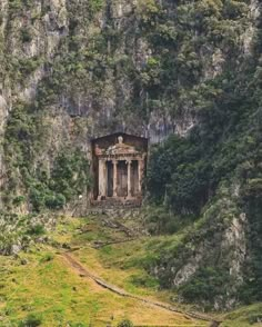 an old building sitting in the middle of a lush green forest covered mountain side area