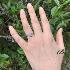 a person's hand with a ring on it and some leaves in the background