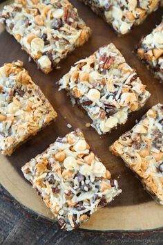 several pieces of dessert sitting on top of a wooden plate with nuts and chocolate toppings