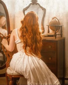 a woman sitting in front of a mirror looking at herself in the mirror with long red hair