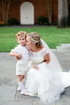 a woman kneeling down next to a little boy in a white suit and tie on