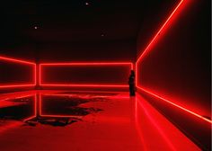 a person standing in an empty room with red lights on the walls and flooring