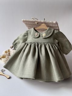 a baby doll is dressed in a green dress and shoes next to a basket with clothes on it