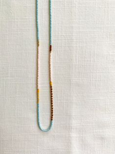 a beaded necklace is laying on a white cloth covered tablecloth with an orange, yellow and blue bead