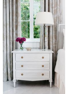 a white dresser sitting next to a window with a lamp on it's side