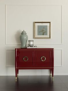 a red sideboard with two drawers and a vase on top in front of a white wall