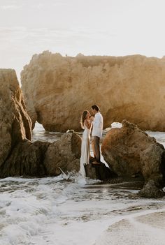 a man and woman standing on rocks in the ocean