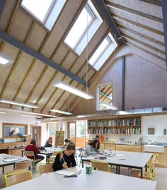 several people are sitting at tables in a room with bookshelves and skylights