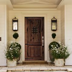 two planters with white flowers are in front of a gray door on a house