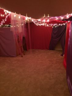 a room with red curtains and lights on the ceiling is lit up by fairy lights