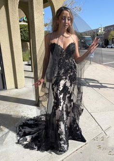 a woman in a black and white dress is standing on the sidewalk with her hands out