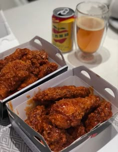 two boxes filled with fried chicken next to a glass of beer on a white table