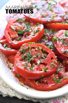 sliced tomatoes on a white plate with herbs and seasoning over the top text reads marinated tomatoes