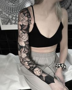 a woman sitting on top of a bed wearing a black and white flower arm tattoo