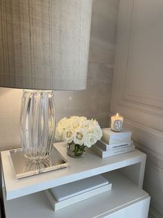 a white table topped with a vase filled with flowers next to a lamp and books