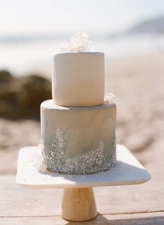 a three tiered cake sitting on top of a wooden table next to the ocean