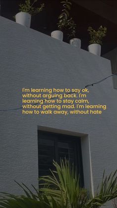 a white building with a poem written on the side and potted plants next to it