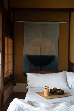 a tray with food on top of a bed in front of a painting hanging above it