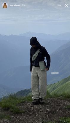 a man standing on top of a lush green hillside with mountains in the back ground