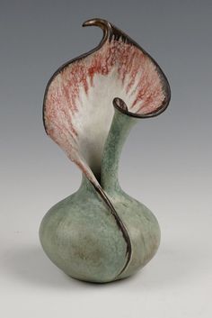 a green vase with red and white designs on the outside, sitting in front of a gray background