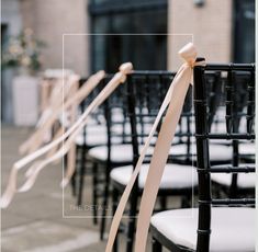 rows of black chairs with ribbons tied to the back of them in front of a building