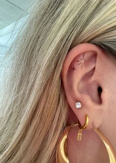 a woman with long blonde hair wearing gold hoop earrings and a star tattoo on her left ear