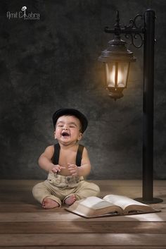 a baby sitting on the floor with an open book in front of him and a lamp