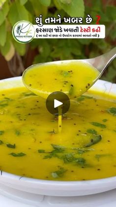 a spoon full of yellow soup in a white bowl with green leaves on the side