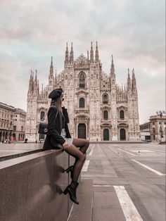 a woman sitting on a ledge in front of a cathedral