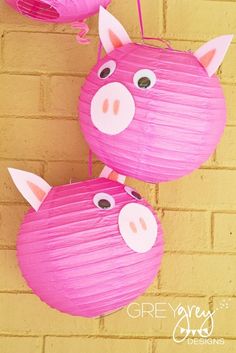 two pink pig paper lanterns hanging from a brick wall