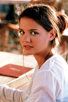 a woman sitting at a table with a book in her hand and looking off to the side