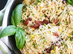 a skillet filled with pasta and vegetables on top of a white towel next to green leaves