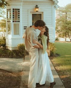 a young man and woman kissing in front of a white house on the sidewalk outside