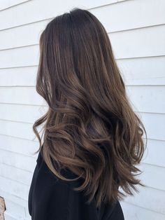 the back of a woman's head with long, wavy hair in front of a white house