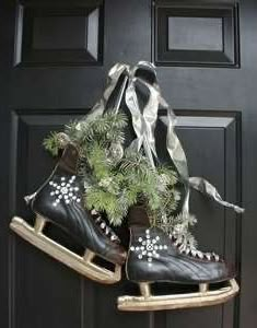 two ice skates are hanging on the front door and decorated with pine cones, evergreen leaves and ribbons