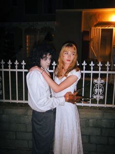 a man and woman dressed up in costumes standing next to each other near a fence