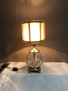 a glass lamp sitting on top of a table next to a white cloth covered wall