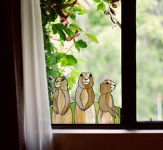 three beavers are sitting on the window sill in front of some plants and trees