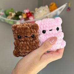 a hand holding two small crocheted teddy bears in front of a shelf full of stuffed animals