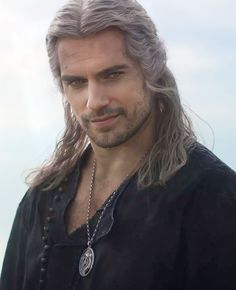 a man with long grey hair wearing a black shirt and silver necklace on his neck