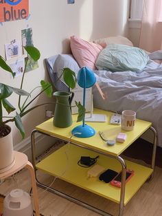 a yellow table topped with a blue lamp next to a green plant and a bed