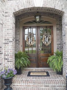 two potted plants sit on the front steps of a brick house with double doors