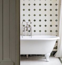 a white bath tub sitting next to a bathroom wall with green and white tiles on it