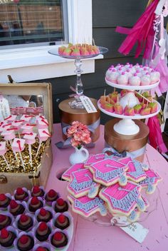 a pink table topped with lots of cupcakes and desserts next to a window