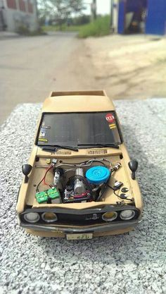 an old model car with its hood open on the ground next to some rocks and gravel